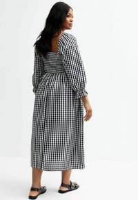 Abito in gingham bianco e nero con maniche a puff, schiena arricciata e lunghezza fino al polpaccio. Indossato con sandali neri flat.