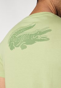 Φωτεινό πράσινο βαμβακερό t-shirt με υφή λογότυπου κροκοδείλου στο πίσω μέρος. Κοντά μανίκια και λαιμόκοψη τύπου crew.