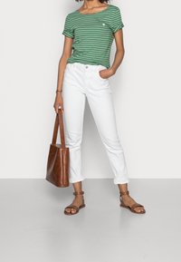 Camiseta a rayas verdes y blancas, jeans blancos con dobladillo, bolso tote de cuero marrón y sandalias planas marrones, exhibidos sobre un fondo liso.