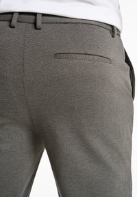 Grijze broek van gemêleerd stof, met een achterzak voorzien van een subtiele naad, gestyled met een riem.