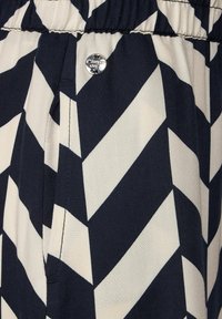 Navy ja koivunvalkoinen kuvioitu kangas, jossa on rohkeat diagonaaliset chevronsuunnat, ja vyötärön lähellä hopeinen painonappi kiinnitystä varten.