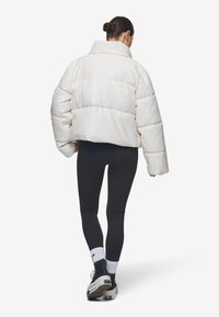 Luftig hvit jakke med høyt krage og brede ermer, med quiltede seksjoner. Kombinert med svarte tights og sneakers.