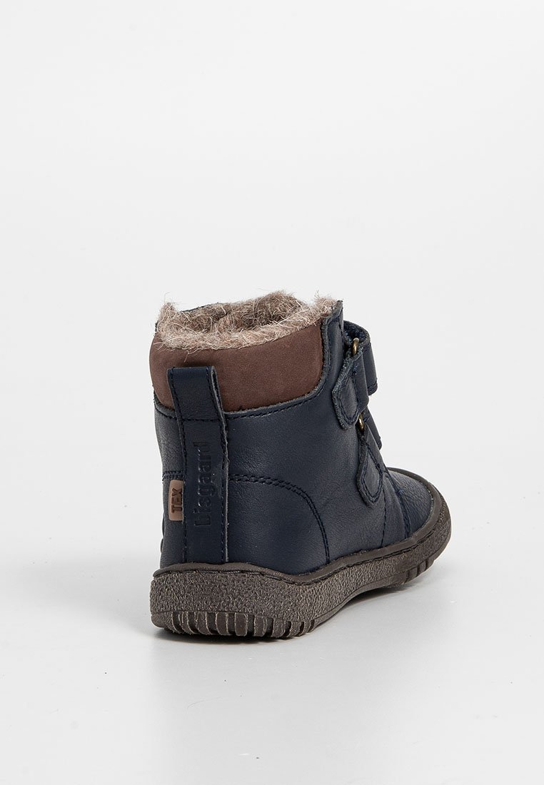 Kinders Winterstiefel in Marineblau mit braunem Besatz, Klettverschlüssen und flauschigem Innenfutter, von der Rückseite auf einem einfachen Hintergrund betrachtet.
