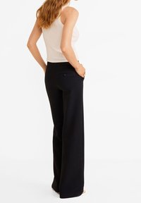 Pantalons noirs à jambe large avec une texture lisse et une poche arrière dotée d'un détail de bouton. Assortis à un débardeur crème à côtes ajusté.