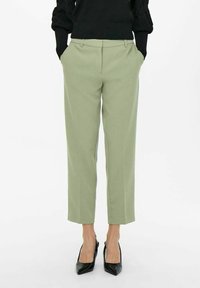 Jasnozielone, dopasowane spodnie z bocznymi kieszeniami i prostym krojem, w zestawieniu z czarnymi, spiczastymi szpilkami. Gładka faktura materiału.