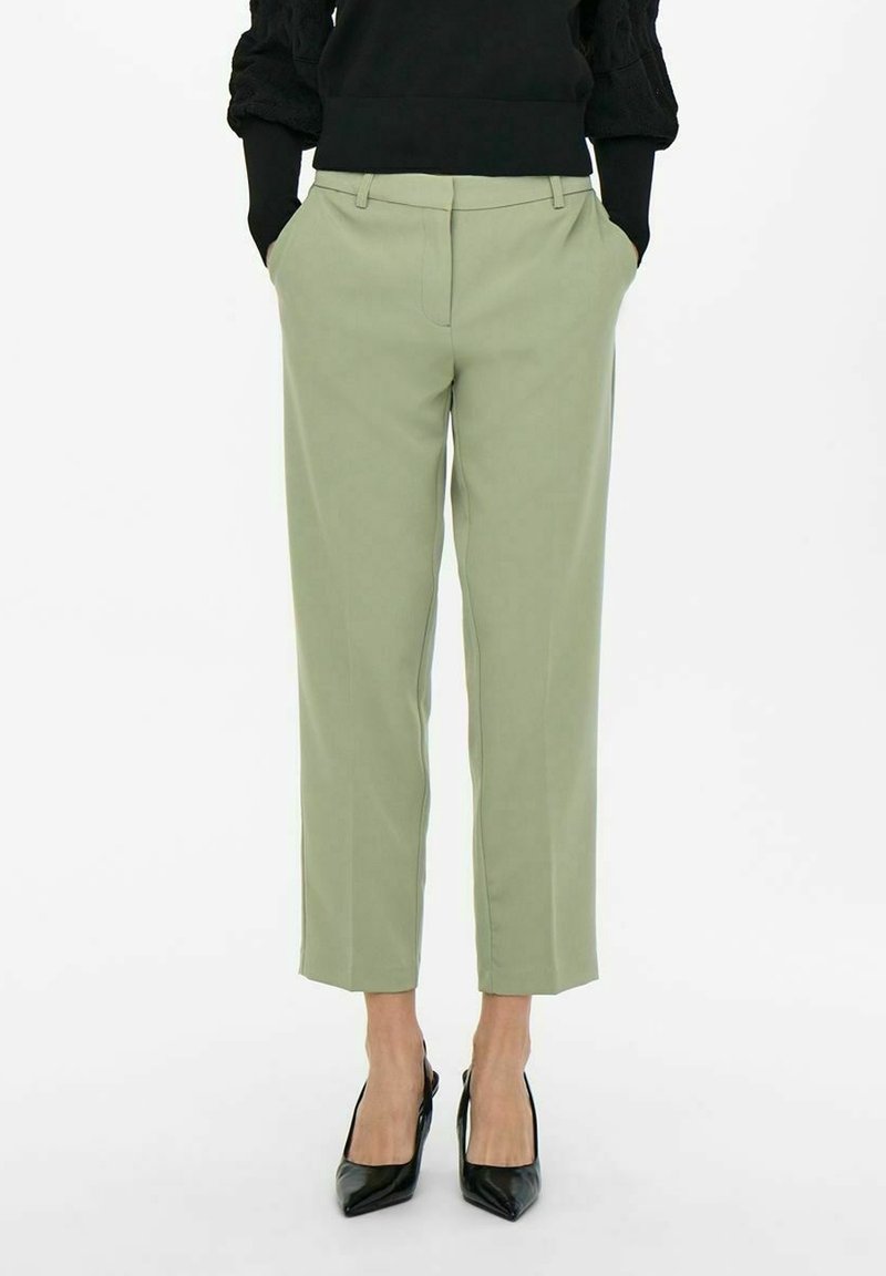Jasnozielone, dopasowane spodnie z bocznymi kieszeniami i prostym krojem, w zestawieniu z czarnymi, spiczastymi szpilkami. Gładka faktura materiału.