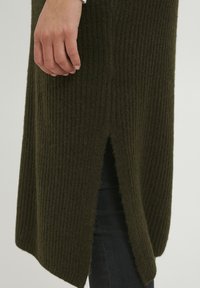 Abito in maglia verde scuro, con texture a coste, spacco laterale e una vestibilità morbida. Il materiale sembra morbido e caldo.