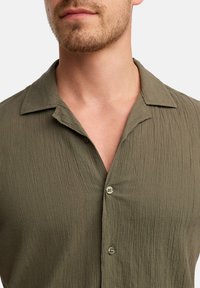 Olijfgroen kortarmsgemengd overhemd met een gestructureerde stof, voorzien van een notched kraag en twee knopen aan de voorkant.