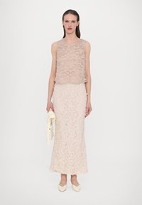 Two-piece outfit featuring a floral embroidered beige sleeveless top and a matching long skirt, both with layered texture, paired with cream heels.
