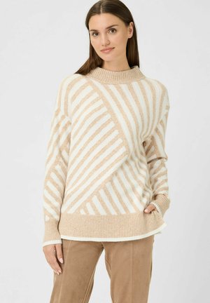 Pull en tricot beige et crème avec des rayures, col montant côtelé, coupe ample et motif texturé, associé à un pantalon en daim tan.