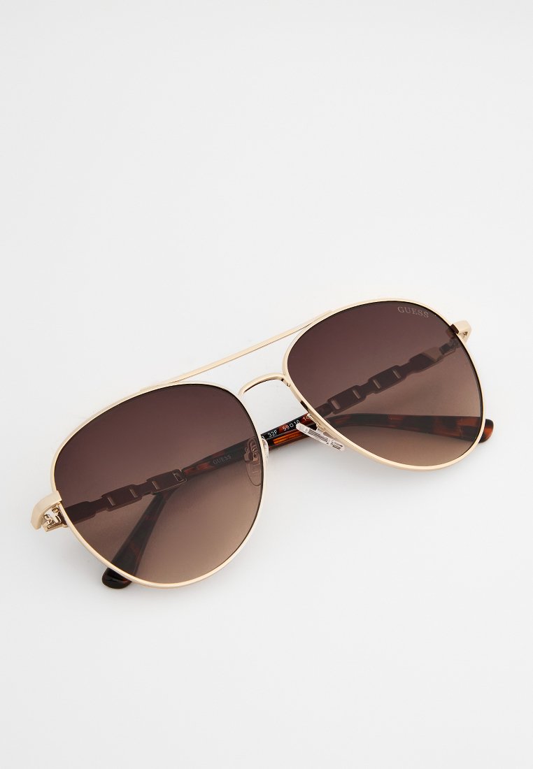 Occhiali da sole stile aviator con montatura in metallo dorato, lenti marroni scure e aste a motivo tartaruga. Includono naselli regolabili.