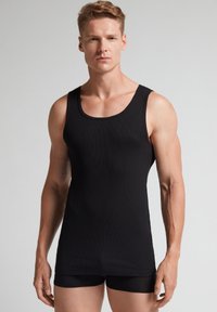 Schwarzes geripptes Tanktop aus elastischem Stoff, mit Rundhalsausschnitt und ärmellosem Design, kombiniert mit schwarzen eng anliegenden Shorts.