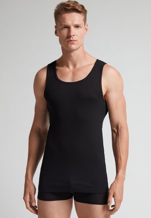 Schwarzes geripptes Tanktop aus elastischem Stoff, mit Rundhalsausschnitt und ärmellosem Design, kombiniert mit schwarzen eng anliegenden Shorts.