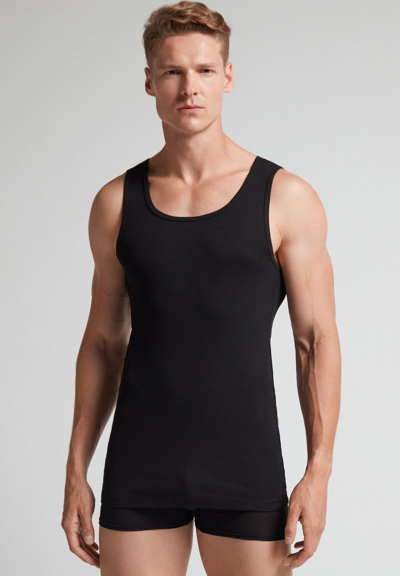 Schwarzes geripptes Tanktop aus elastischem Stoff, mit Rundhalsausschnitt und ärmellosem Design, kombiniert mit schwarzen eng anliegenden Shorts.