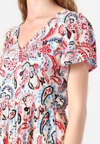 Floral-patterned dress in soft fabric featuring a V-neck, short sleeves, and a gathered waist. Colors include red, blue, and cream.