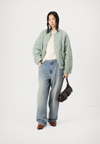 Polstret mintgrønn bomberjakke med et teksturert mønster, kremhvit genser, oversized lyseblå jeans og en mørkebrun håndveske. Brune sko.