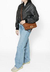 Borsa a tracolla in pelle marrone texturizzata con chiusura in oro, abbinata a una giacca bomber in pelle nera e jeans a pacco leggeri di colore blu chiaro.