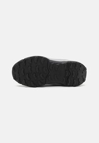 Black hiking shoe sole featuring deep, rugged tread patterns for traction, with a smooth midsole transition and reinforced heel.