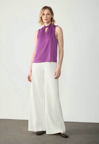 Top roxo sem mangas com decote tipo buraco da fechadura, combinado com calças largas brancas. O tecido suave e o corte descontraído completam o visual.
