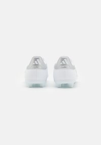 Balti Adidas Copa Pure futbolsneki ar sudrabainiem papēža uzgaļiem, uz kuriem redzama zīmola logo, skatīti no aizmugures uz baltas fona.