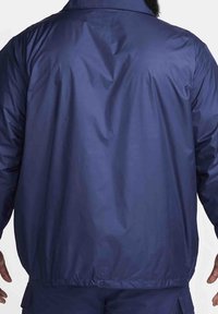 Marinblå lättvikts vindjacka med en slät, glänsande yta, elastiska ärmslut och midja utan synliga logotyper eller dekorationer.