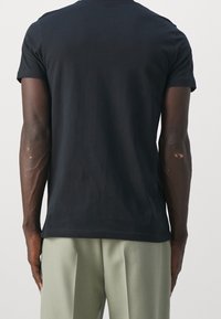 Czarna koszulka z krótkim rękawem wykonana z miękkiej bawełny, o klasycznym kroju i prostym designie, zestawiona z jasnoszarymi spodniami plisowanymi.