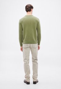 Zöld kötött pulóver kerek nyakkal, hosszú ujjakkal és texturált felülettel, világos bézs színű egyenes szárú nadrággal és fekete cipővel párosítva.