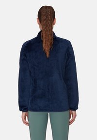 Pullover in fleece blu navy con superficie strutturata, maniche lunghe e colletto alto. La parte posteriore presenta un orlo arrotondato e liscio.