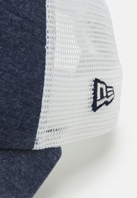 Gorra azul marino con una parte trasera de malla blanca. Presenta un diseño estructurado y un logo bordado en el lateral, que muestra una mezcla de materiales.
