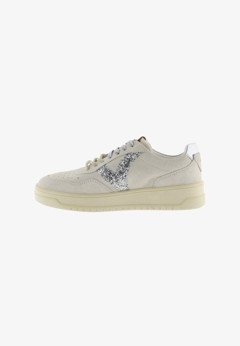 Beige suède sneaker met lichtbeige zool, zilverkleurig glinsterend ruitjesontwerp aan de zijkant, geperforeerde neus en zilveren accenten op het hielstuk.