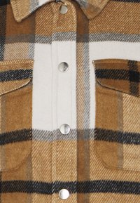 Ruutukuvioinen ruskea ja valkoinen flanellipaita, jossa on pehmeä pinta, hopeiset nepparit ja kaksi rintataskua.