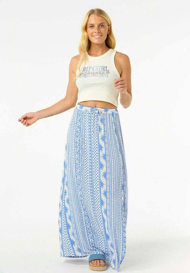 Jupe maxi bleu clair avec des motifs géométriques blancs, dotée d'une taille élastique avec cordon de serrage. Associée à un débardeur blanc court et des sandales.