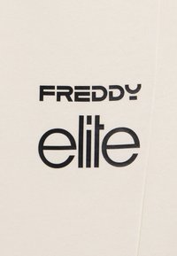 Tessuto crema con testo stampato in nero "FREDDY" sopra "elite." Design del font semplice e moderno con texture liscia, senza grafiche aggiuntive.
