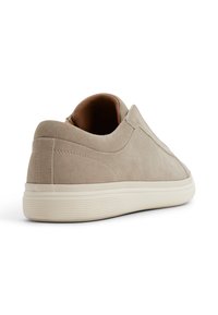 Beżowe zamszowe sneakersy o gładkiej fakturze, niskim profilu, elastycznych bocznych panelach i kremowej gumowej podeszwie z delikatnymi poziomymi liniami.