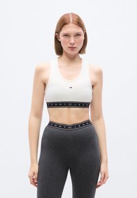 Λευκό αθλητικό σου τιέν με μαύρη λωρίδα που φέρει το λογότυπο «TOMMY JEANS», συνδυασμένο με γκρι κολάν. Ομαλή υφή και εφαρμοστή σχεδίαση.