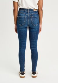 Jeans skinny bleu, taille haute, avec un design classique à cinq poches, des coutures contrastées et une étiquette sur la taille.
