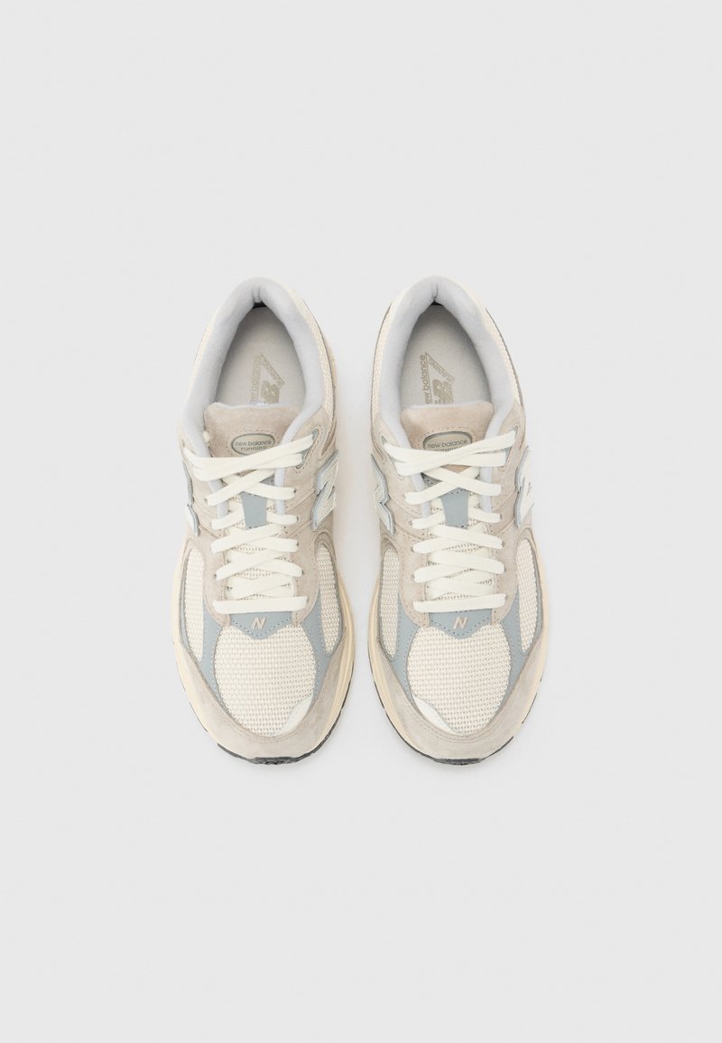 Des chaussures de sport beige et bleu clair avec une tige en mesh, des accents en daim, une semelle épaisse et des lacets blancs, arborant un logo 'N' bien en vue sur le côté.