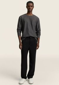 Hall värviline pika varrukaga särk rinnataskuga, kombineeritud mustade pükste ja valgete tossudega. Neutraalne taust rõhutab riietuse värve.