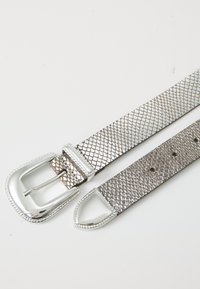 Ceinture en acier argenté avec un motif en filet texturé, dotée d'une boucle brillante en argent et de pointes effilées à chaque extrémité.