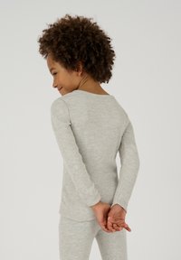 Top grigio a maniche lunghe con texture rigata e scollatura rotonda, indossato con pantaloni abbinati, realizzato in un tessuto morbido e texturizzato. Le mani del bambino sono incrociate dietro la schiena.