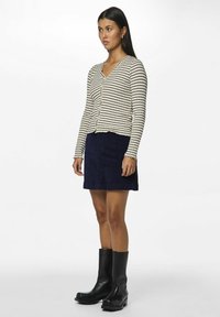 Cardigan en tricot rayé crème et marine, associé à une mini-jupe en velours côtelé bleu foncé et des bottes à talons carrés en cuir noir.