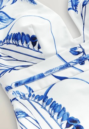 Hvidt stof med blå blomstermønstre; har en glat tekstur og tydelige linjer med et struktureret design og detaljerede accenter.