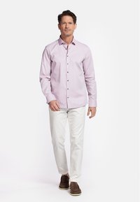 Lichtroze overhemd met donkere knopen, lange mouwen, gecombineerd met witte broek en bruine loafers, staande op een effen achtergrond.