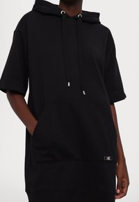 Czarna bluza z kapturem o krótkich rękawach, z przednią kieszenią oraz srebrnymi metalowymi akcentami na troczkach i detalu logo.