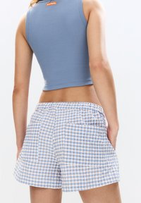 Modrý žebrovaný crop top s oranžovou nášivkou, v kombinaci se světle modrými a hnědými kostičkovanými šortkami s dvěma zadními kapsami a elastickým pasem.