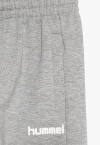 Grijze sweatpants van zacht materiaal met een elastische tailleband. Voorzien van een zijzak en witte merktekst op het linkerbeen.