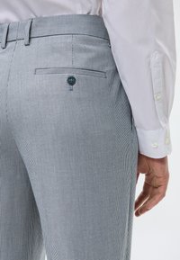 Γκρι και λευκό καρό παντελόνι με slim fit, που διαθέτει πίσω τσέπη και λεπτομέρεια με κουμπί, συνδυασμένο με ένα ανοιχτόχρωμο πουκάμισο.