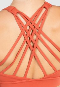 Top deportivo con espalda nadadora en color coral con tirantes entrecruzados. La tela es suave y elástica, destacando el diseño de la espalda.