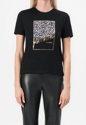 Frau trägt ein schwarzes T-Shirt mit einem goldgerahmten Leopardenmuster-Quadrat und den Worten "femme future" in goldener Schrift.