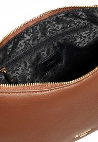 Binnenkant van een bruine leren tas met een gouden rits, voorzien van een zwart patroon voering en een klein ritsvakje. Merklabel zichtbaar binnenin.